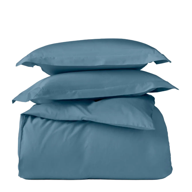 Two blue pillows rest atop the folded Classic Organic Sateen Duvet Set by Coyuchi, all displayed against a plain white background.