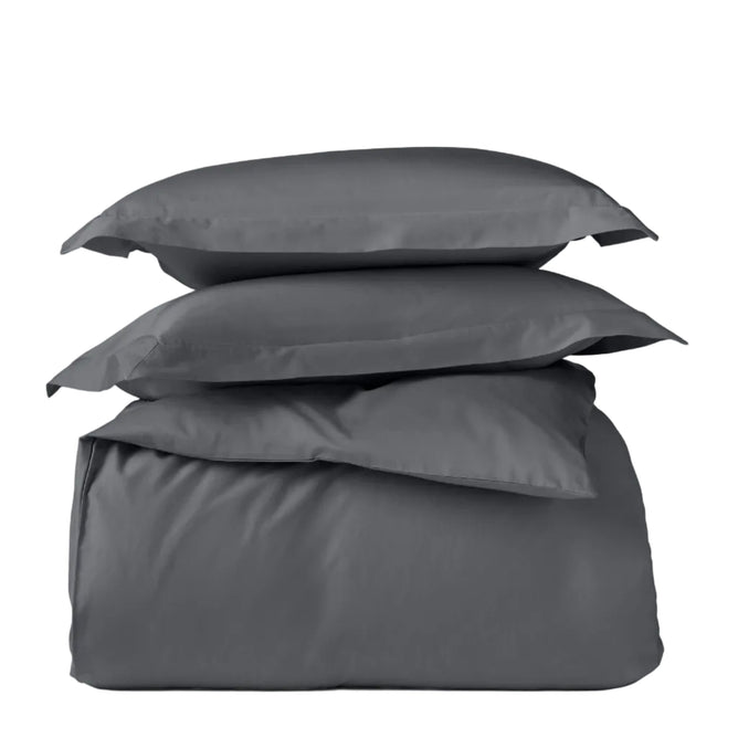 A stack of Coyuchi’s Classic Organic Sateen Duvet Set in dark gray, featuring two pillows on top and a neatly folded duvet made from organic cotton at the bottom, displayed against a plain white background.