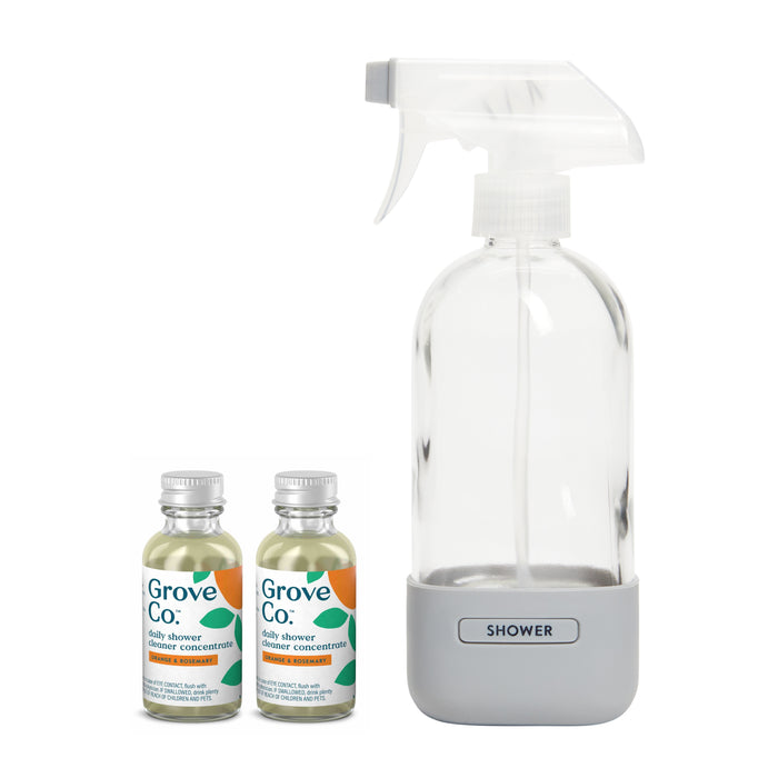 Daily-shower-cleaner-spray-bottle from Grove Collaborative includes a clear spray bottle with a gray base labeled Shower, and two small concentrate bottles with white caps, featuring green and orange label accents.