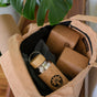 The Yoloha Yoga Cork Tote Bag stylishly holds a stainless steel bottle with a bamboo lid, two cork yoga blocks, and a rolled yoga mat secured in its convenient mat holder, with a large green plant leaf peeking above the bag.