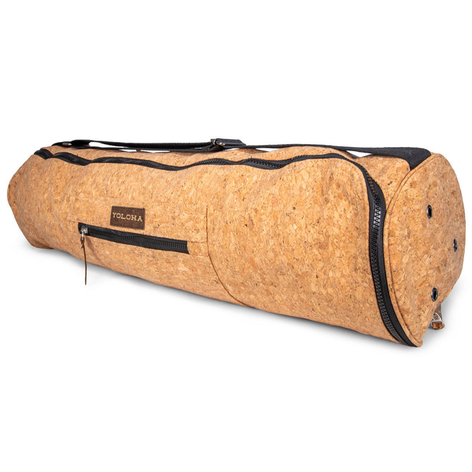 The Cork Yoga Mat Carrier by Yoloha Yoga is a cylindrical bag made from natural cork, featuring a zipper pocket, black handle, and the Yoloha Yoga brand label on the side.