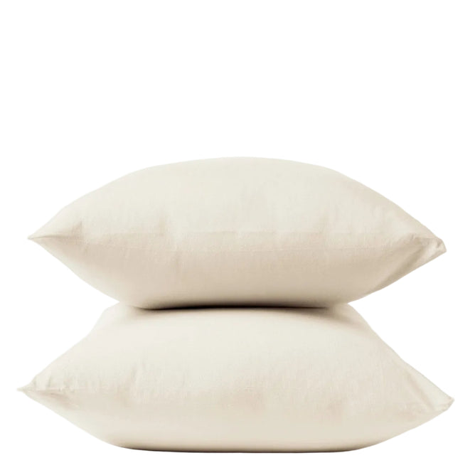 Two cream-colored pillows stacked atop one another against a plain white background, each adorned with Coyuchi Organic Crinkled Percale™ Pillowcases for a touch of breathable bedding luxury.