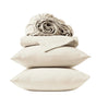 Two beige pillows are stacked atop one another, topped with a folded Coyuchi Organic Crinkled Percale™ Sheet Set and a rolled-up fitted sheet—all crafted from breathable bedding—set against a plain white background.
