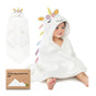 A smiling baby sits wrapped in a white hooded towel designed as a unicorn, with a yellow horn, colorful ears and mane. The towel package and a folded towel are also shown nearby.