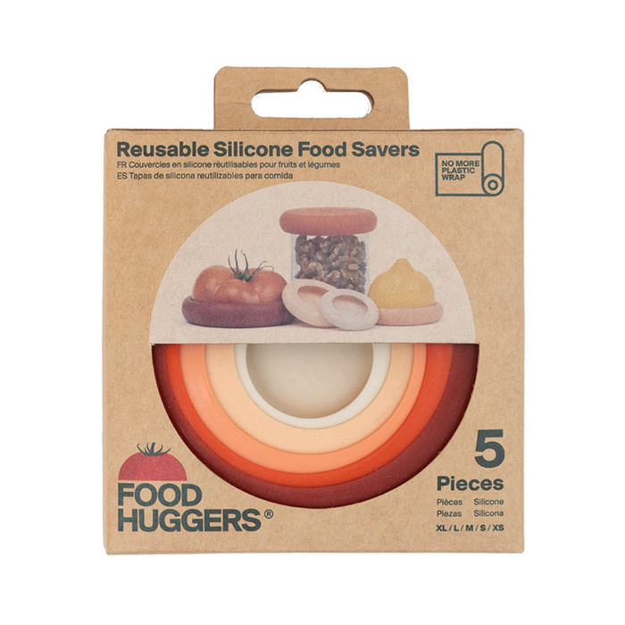 A box of Food Huggers reusable silicone food savers, showing five circular, multicolored lids in orange, yellow, and cream shades, with illustrations of fruit, vegetables, and nuts on the packaging.