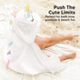 A child sits on sand wearing a white hooded towel designed like a unicorn, with a yellow horn, ears, flowers, and colorful spikes. Text reads: Push the cute limits. Perfect for bath time, poolside & beach fun.