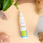 A bottle of Oxyfresh Dental Spray lies on a beige surface surrounded by pet toys, a plant, and a striped cloth. The spray bottle has a white label with blue, green, and orange accents.
