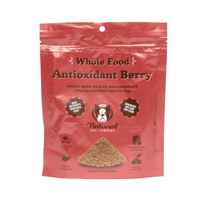 A red resealable bag labeled Whole Food Antioxidant Berry by Natural Dog Company, featuring a cartoon dog. The packaging highlights benefits for dog health and longevity and shows an image of the powdered product.