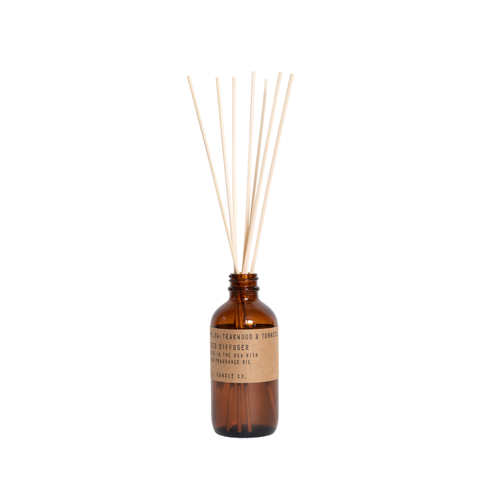 A brown glass bottle with a kraft paper label holds several reed diffuser sticks standing upright, used for dispersing fragrance. The background is plain white.