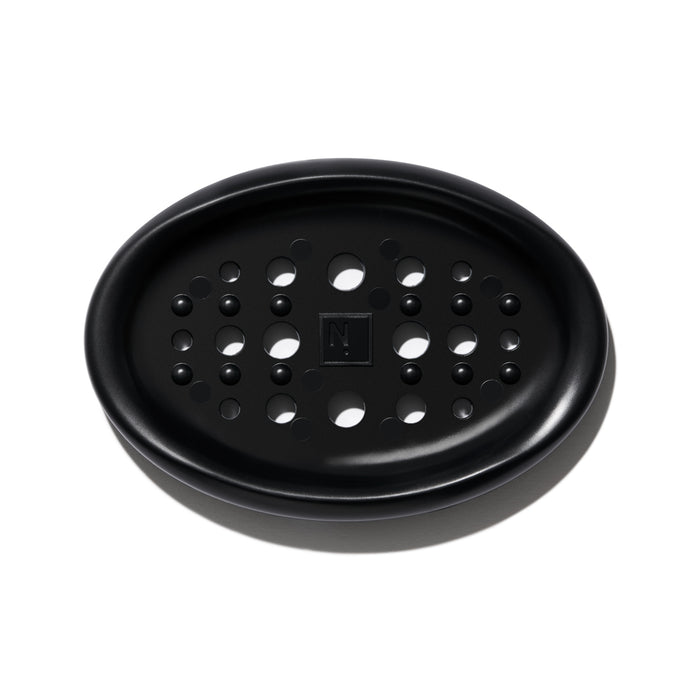 A black oval soap dish with multiple round drainage holes and a raised square in the center, photographed on a white background.