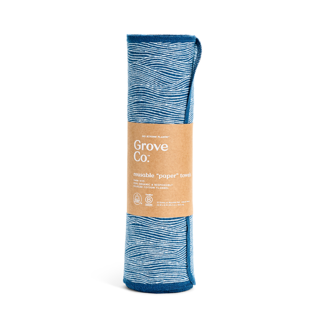 A blue reusable kitchen towel from Grove Co., made of organic cotton flannel, features a white wave pattern and comes rolled with a brown paper label. The Reusable Paper Towels label notes its absorbency, sustainability, and machine-washable attributes.