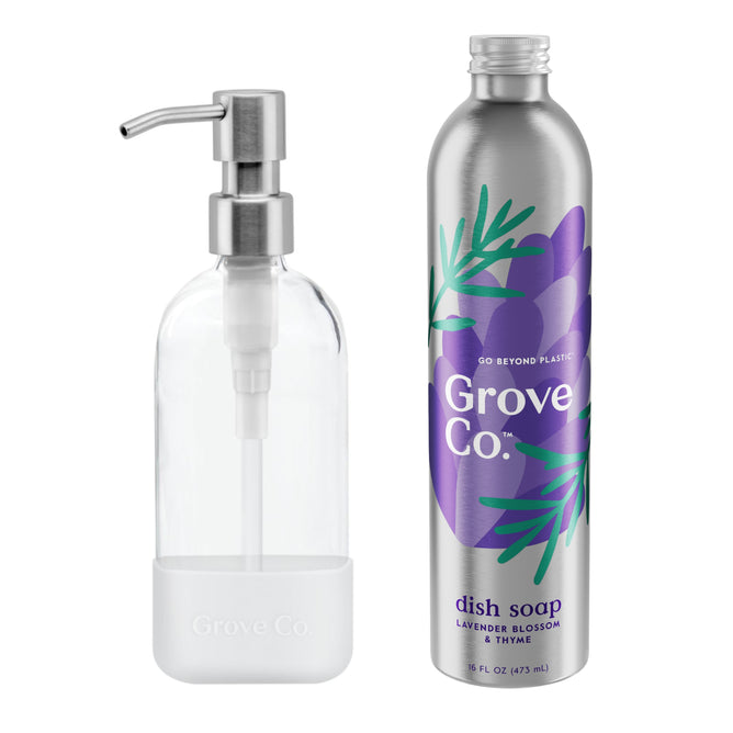 A clear pump bottle elegantly stands next to a metallic Grove Co. Dish Soap Starter Set bottle, featuring a lavender blossom and thyme design, highlighting the brands dedication to reducing plastic waste.