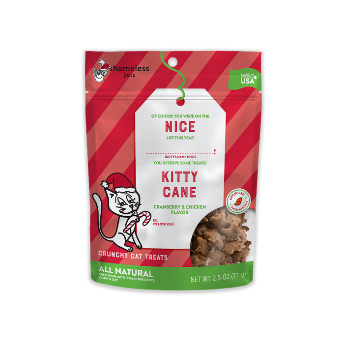 The red packaging of Shameless Pets Kitty Cane Crunchy Cat Treats, Nice List features diagonal stripes and a cartoon cat with a candy cane. These USA-made, natural treats have cranberry & chicken flavors with upcycled sweet potatoes and are available in a 2.5 oz pack.