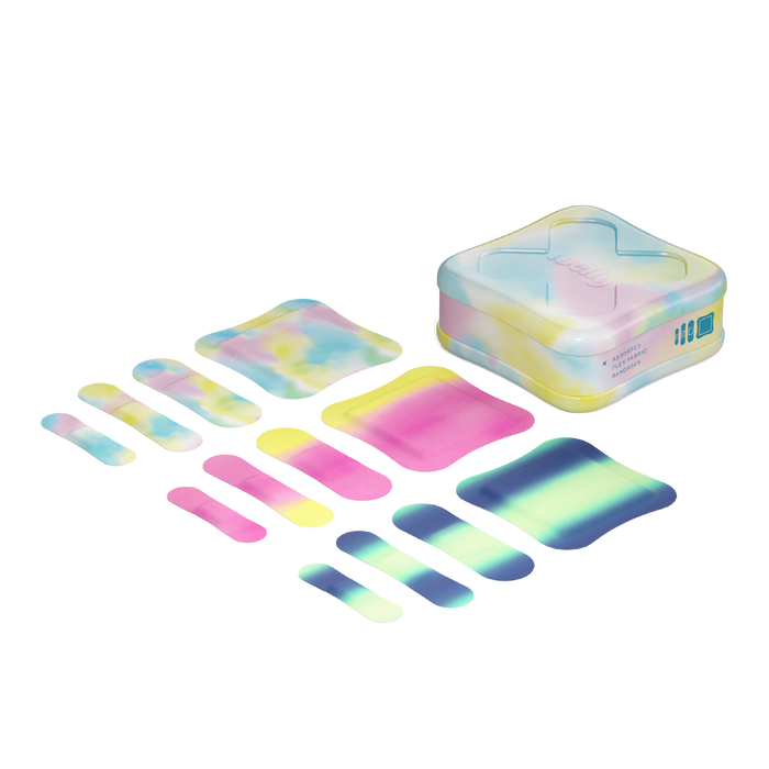 A set of colorful, tie-dye patterned adhesive bandages in various sizes is displayed next to a matching square storage tin with a translucent lid. The bandages and tin have pastel shades of pink, yellow, blue, and green.