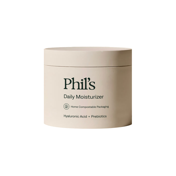 A beige jar labeled Phil's Daily Facial Moisturizer with hyaluronic acid and prebiotics features text about home compostable packaging. The minimal, modern container design appears against a white background.
