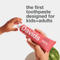 A child’s hand and an adult’s hand hold a red tube of Davids Kids + Adults Premium Toothpaste; text above reads, “the first fluoride free toothpaste designed for kids and adults.”.