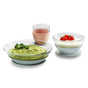 Three glass dishes: one with green puree and parsley garnish, one with pink smoothie in a cup, and one with yogurt topped with strawberries. All dishes are on white backgrounds.