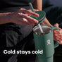 A person opens a green insulated tumbler with a straw, with the words Cold stays cold printed at the bottom of the image.