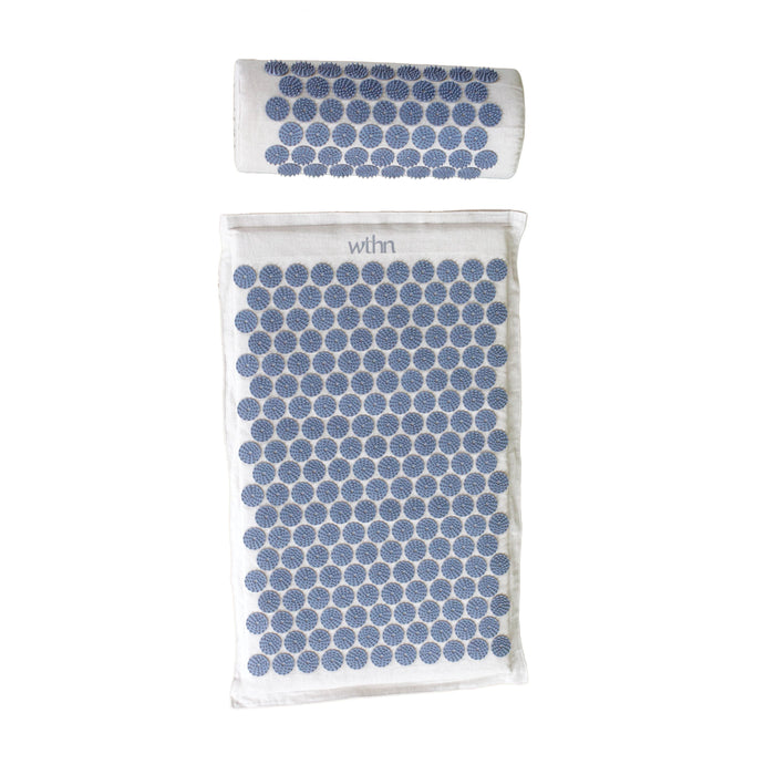 A white acupressure mat and pillow set, both covered with evenly spaced blue circular spikes, laid out on a white background. The mat features the word withn at the top.