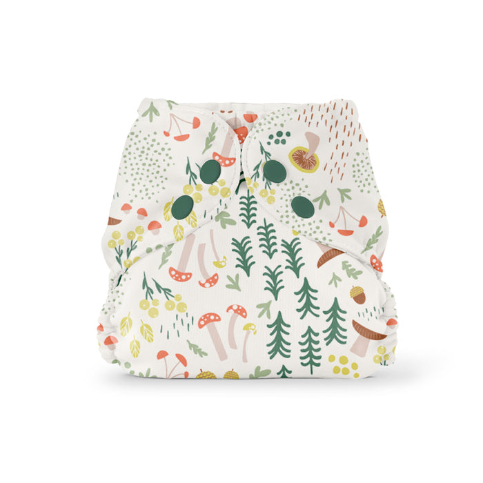 Cloth diaper with a whimsical forest pattern featuring mushrooms, trees, leaves, and berries in green, red, and yellow on a white background, secured with green snaps.