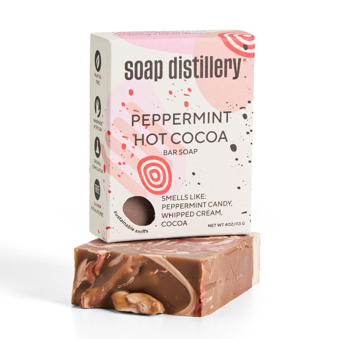 A bar of Soap Distillery Peppermint Hot Cocoa soap sits in front of its box, which is white with pink and brown design elements and text describing the scent as peppermint candy, whipped cream, and cocoa.