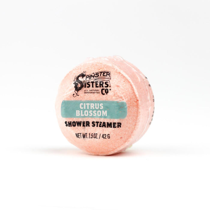 A round, pink shower steamer labeled Citrus Blossom from Spinster Sisters Co. is wrapped in clear plastic with text indicating it weighs 1.5 oz (42 g).