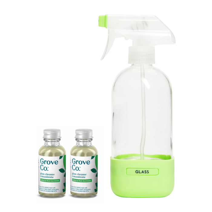 Clear spray bottle with green base labeled Glass next to two Grove Collaborative glass cleaner concentrate bottles, both featuring matching green labels and leaf graphics.