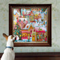 A small dog with a spotted ear gazes up at a framed eeBoo Piece & Love Holiday Village 1000 Piece Puzzle, featuring people skating and festive houses, displayed on a patterned wallpapered wall.