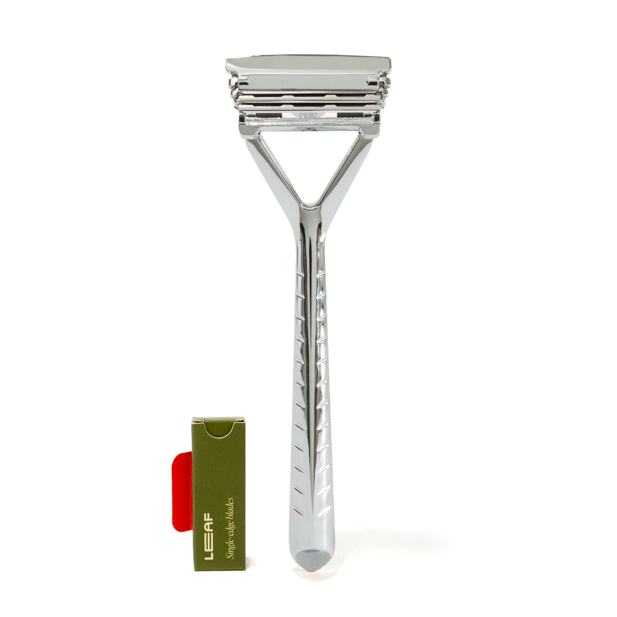 The Leaf Shave Plastic Free Razor is a sleek, polished safety razor with all-metal construction and a textured handle, ideal for sensitive skin. It stands upright next to a green and red box holding replacement blades.