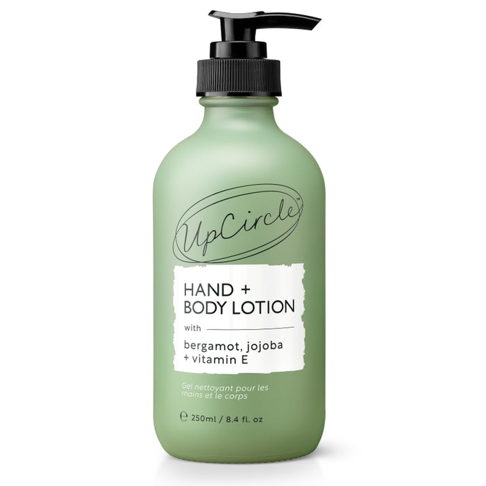 A green 250ml pump bottle of UpCircle Hand + Body Lotion, featuring bergamot, jojoba, and vitamin E, with black text on a white label and a black pump dispenser.