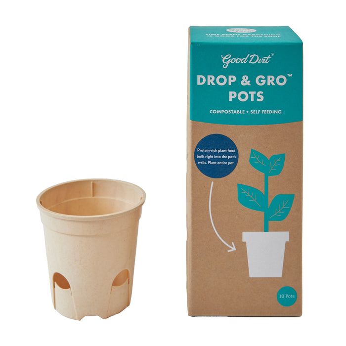 A compostable plant pot sits next to its packaging, which reads Good Dirt DROP & GRO POTS and shows an illustration of a plant growing in a pot. The box also states compostable and self feeding.