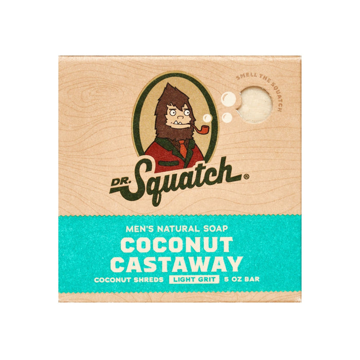 Square box of Dr. Squatch mens natural soap, Coconut Castaway scent. The packaging features a cartoon sasquatch, product name, and a smell hole. Text highlights coconut shreds, light grit, and 5 oz bar size.