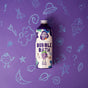 A bottle of Pacha Soap Co. Kids Bubble Bath in Berry Grape scent stands upright on a purple background decorated with playful, child-like drawings in blue crayon, including flowers, stars, a UFO, grapes, and question marks.