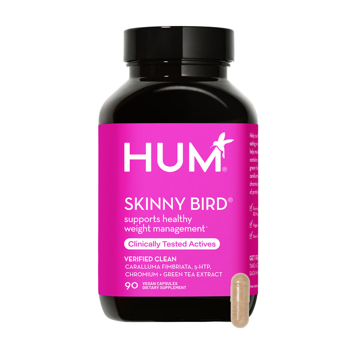 A black bottle with a bright pink label for HUM Skinny Bird dietary supplement, featuring text about weight management support and ingredients. A single light brown capsule is shown in front of the bottle.