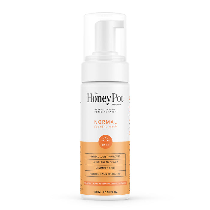 A bottle of The Honey Pot Company Normal Foaming Wash with an orange label, featuring text about its gynecologist approval, pH balance, and gentle, non-irritating formula. The bottle has a clear cap and pump top.