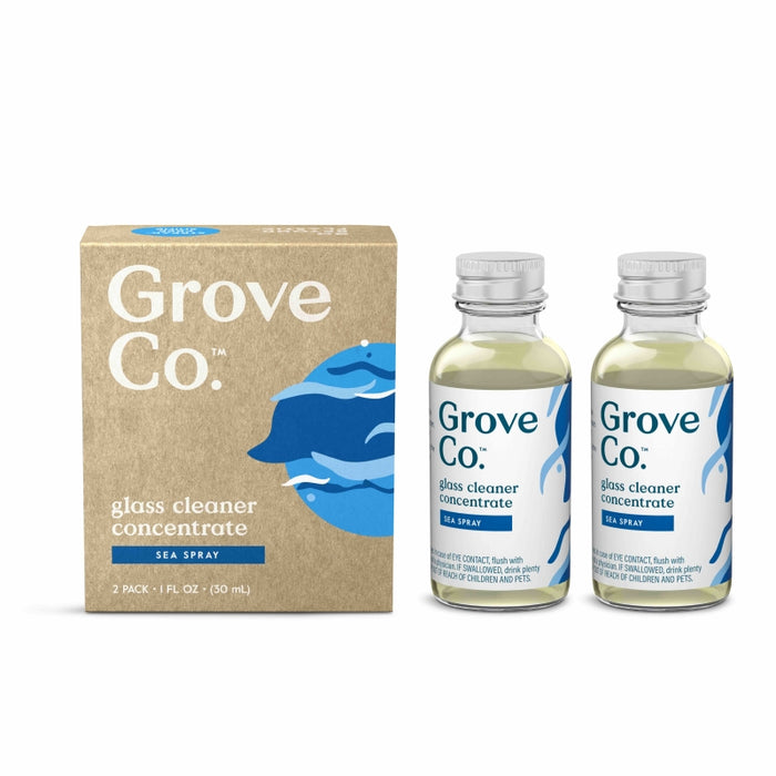 Two bottles of Grove Co. glass cleaner concentrate in Sea Spray scent stand next to a brown and blue box with the same branding and design. The packaging features blue waves and clear labeling.