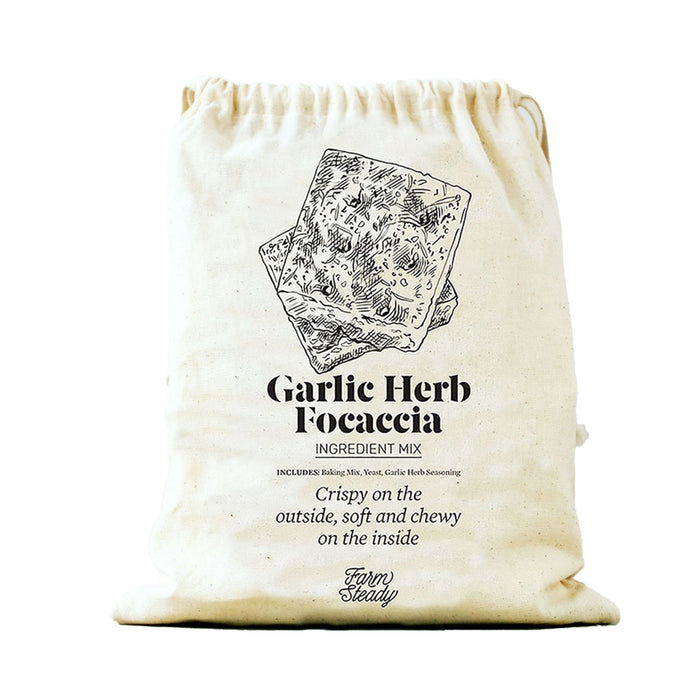 A beige cloth bag labeled Garlic Herb Focaccia Ingredient Mix with an illustration of focaccia slices. Text describes the bread as crispy outside and chewy inside. The brand name Farm Steady appears at the bottom.