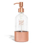 The Grove Co. Refillable Dish Soap Dispenser features a transparent body with a bronze pump and base, adorned with a leaf and fruit design. It adds elegance to your sustainable home, reducing plastic waste while sitting beautifully against any plain white backdrop.
