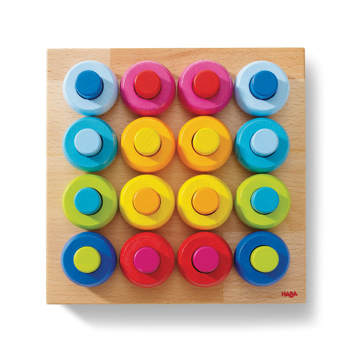 A wooden board with a 4x4 grid of colorful circular pieces in pairs of two, each pair featuring a large and small circle in matching colors: blue, pink, yellow, green, red, and orange.