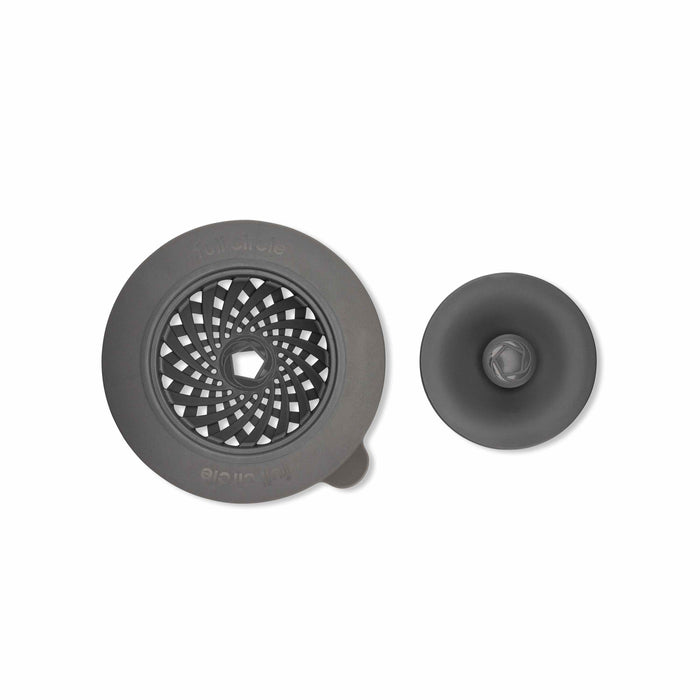 Two gray kitchen sink accessories: a round strainer with a geometric cutout pattern and a small tab, and a matching stopper with a smooth, domed surface, both on a white background.