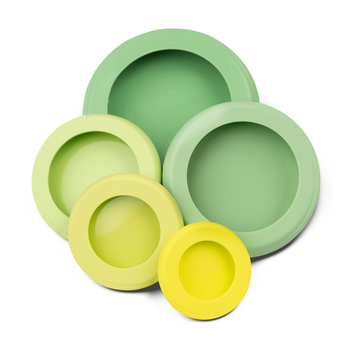 Four round silicone lids in different sizes and shades of green and yellow are arranged overlapping each other on a white background.