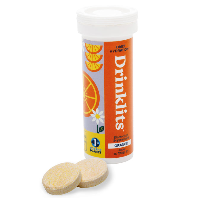 A tube labeled Drinklits Daily Hydration—Orange Flavor with images of orange slices stands upright. Two round effervescent tablets are placed in front of the tube.