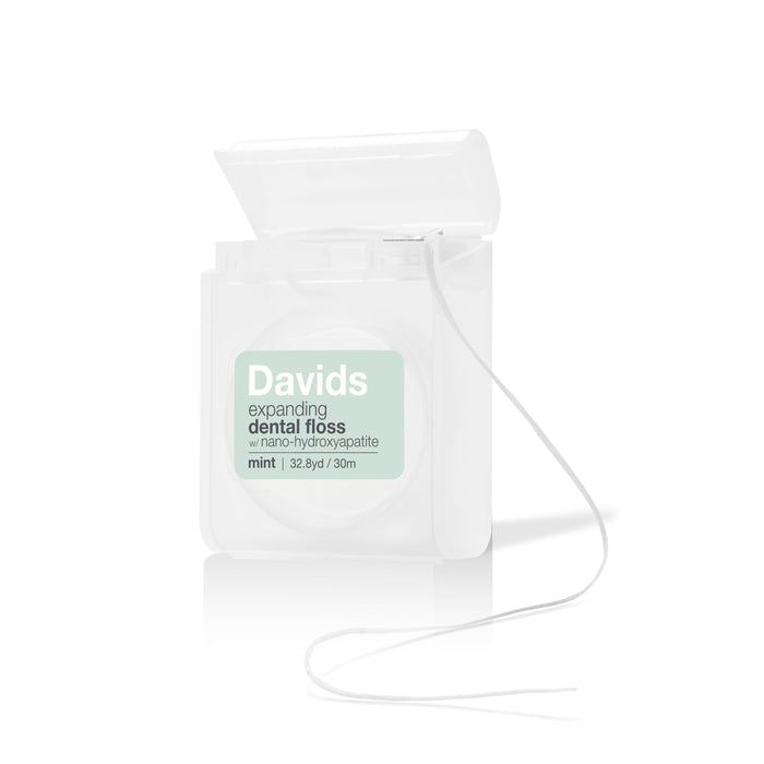 A white container of Davids mint expanding dental floss with the lid open and floss partially pulled out, showing the label with product details on the front.