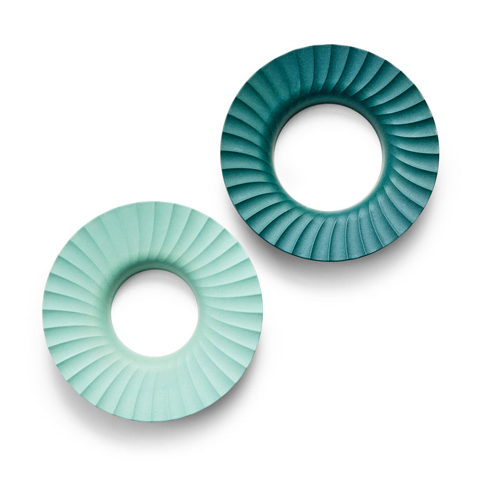 Two circular objects with a central hole and a spiral, ridged design. One is light green, the other is dark teal. They are positioned diagonally on a white background.
