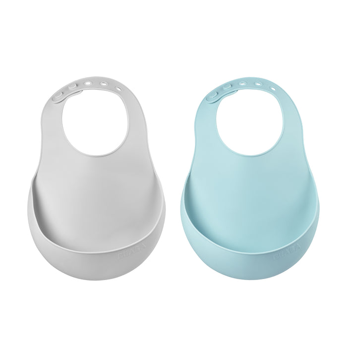 Two silicone baby bibs with adjustable neck fasteners, one in light gray and one in light blue, each featuring a deep pocket at the bottom to catch food spills.