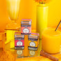 The Spicewalla Golden Milk Collection, featuring three spice tins, is displayed on a yellow backdrop alongside a glass of golden milk, a cinnamon stick, flowers in a yellow vase, and turmeric powder.