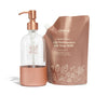 A clear glass soap dispenser with a rose gold pump and base sits next to a refill pouch labeled Grove High Performance Dish Soap Refill, Apple Spice. Both items are in coordinating rose gold tones.