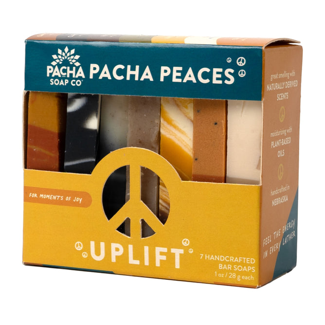 A Bar Soap, Pacha Peaces variety pack by Pacha Soap Co. stands upright, showing colorful soap bars. The packaging includes a peace symbol and Uplift, highlighting handcrafted, plant-based soaps with natural scents.