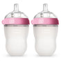 Two silicone baby bottles with clear nipples and pink rings, labeled comotomo. The bottles have a frosted, ergonomic design and are standing upright side by side against a white background.
