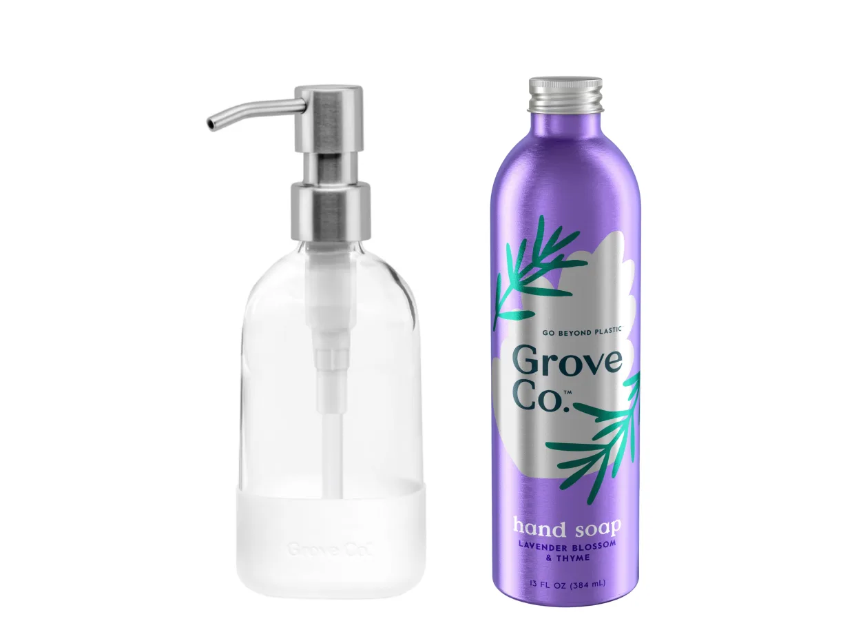 Clear glass pump dispenser bottle next to a purple aluminum bottle labeled Grove Co. hand soap, lavender blossom & thyme. The bottles are upright on a white background.